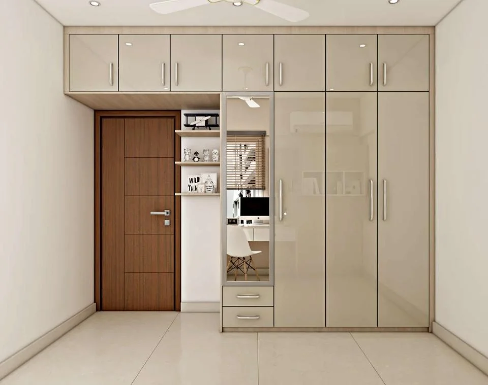 Beige glossy wardrobe with mirror, overhead cabinets, and small workspace in a modern bedroom.