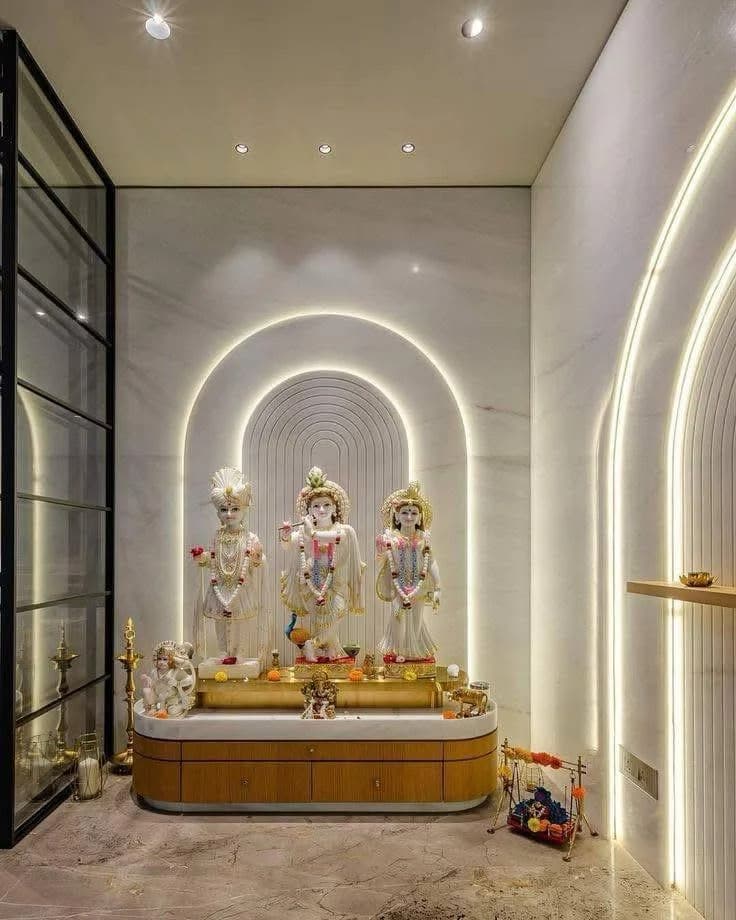 Modern pooja room featuring marble deity statues, arched wall with LED lighting, and wood altar.