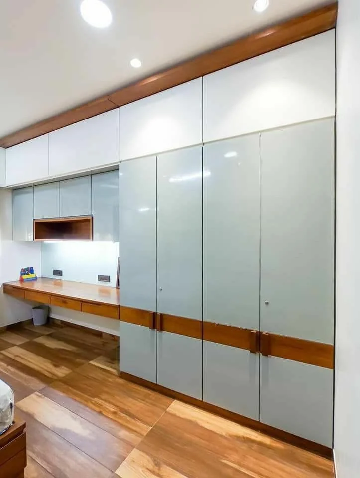 Modern built-in wardrobe and floating desk in a bedroom with light gray doors and wood accents.