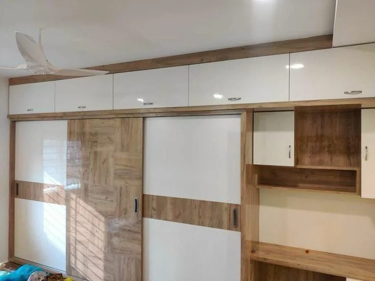Modern wardrobe with white and wood sliding doors and overhead cabinets.